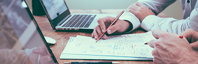 Person Writing on Paper beside Laptop